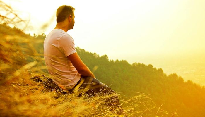 Person meditating outdoors at sunrise, looking calm and peaceful.